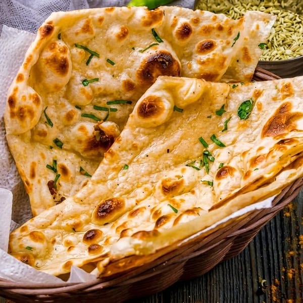 Basket of golden naan bread with herbs, alongside bowls of spices and dried chilies.