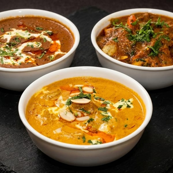 Three bowls of Indian curries, two brown and one orange, garnished with cream, herbs, and nuts.
