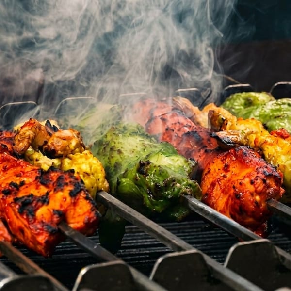 Skewers of colorful marinated chicken and vegetables grilling with smoke rising.